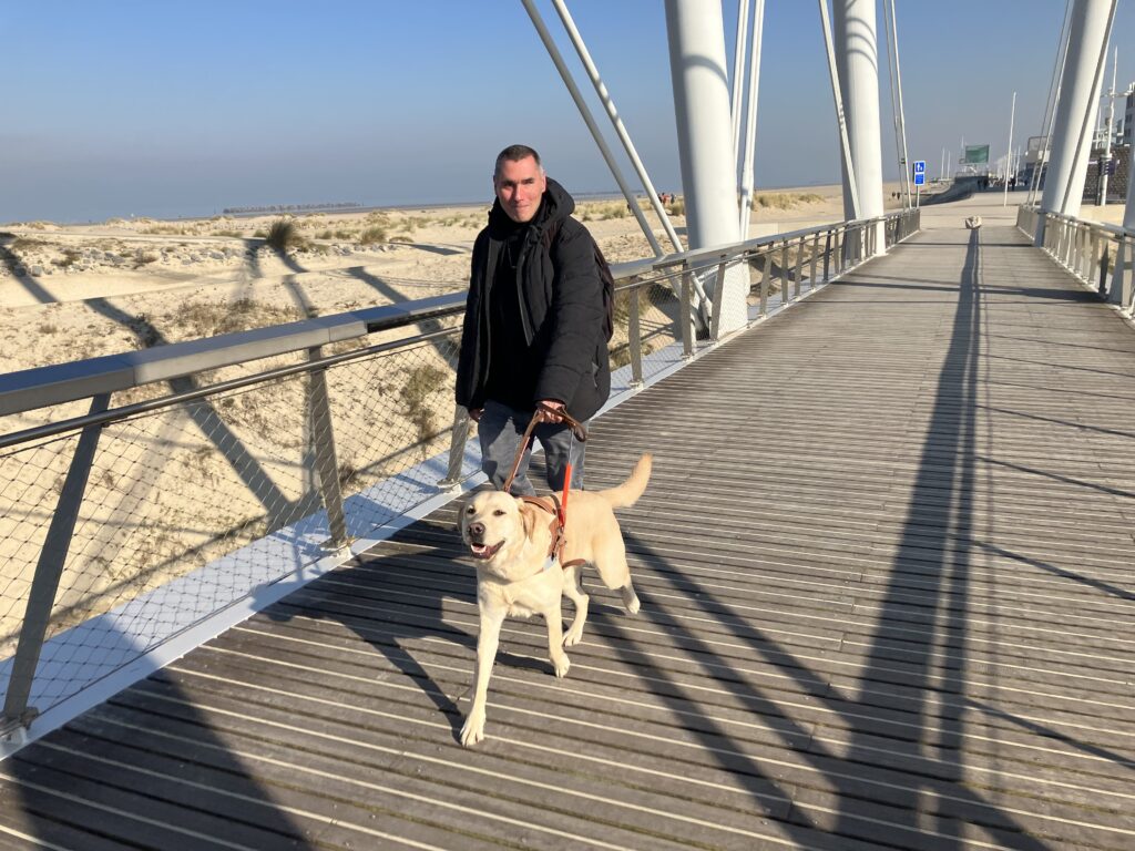 Remise de Sanka - un homme marche sur la digue avec son chien guide labrador sable